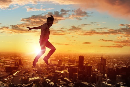 Silhouette of dancer jumping against city in lights of sunriseの写真素材