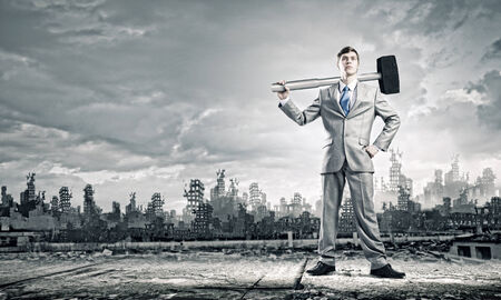 Young businessman with hammer and ruins at backgroundの写真素材