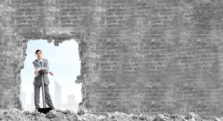 Young businessman with big hammer against wallの写真素材