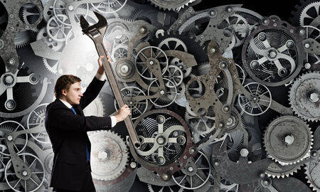 Young businessman fixing gears mechanism with wrenchの写真素材