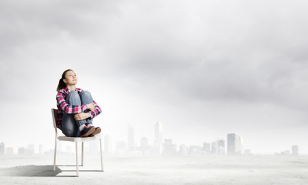 Young girl sitting in chair against city backgroundの写真素材