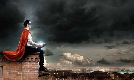 man in cape and mask sitting on top of building and reading bookの写真素材