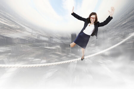 Young businesswoman balancing on rope above cityの写真素材