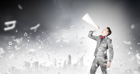 Young excited businessman screaming in paper trumpetの写真素材