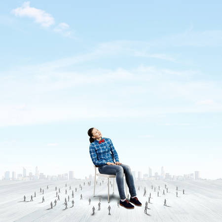 Woman in casual sitting on chair and many small silhouettes of businesspeople aroundの写真素材