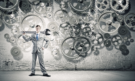 Young businessman with wrench against mechanism backgroundの写真素材