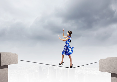 Young woman in blue dress walking on rope above gapの写真素材