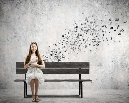 Young pretty asian woman sitting on bench and reading bookの写真素材