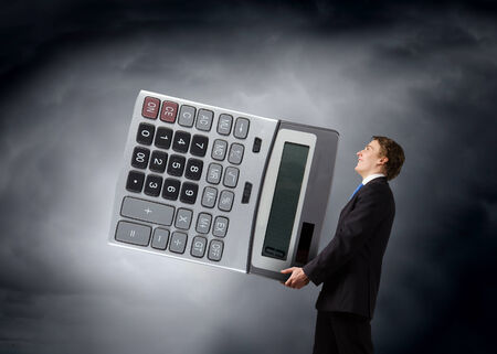 Young businessman in suit carrying big calculatorの写真素材