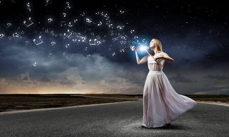 Young woman in white dress playing violin at nightの写真素材