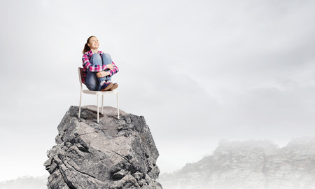 Young woman in casual sitting in chair on top of rockの写真素材