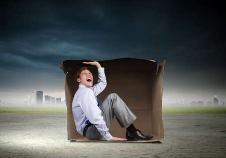 Young frustrated businessman sitting in small carton boxの写真素材