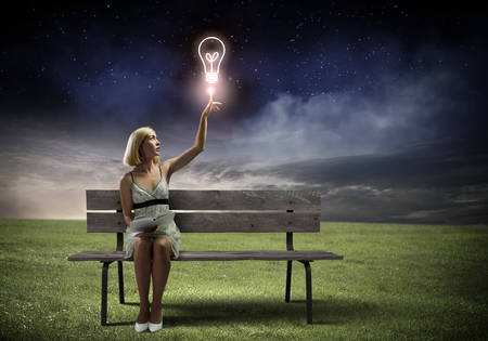 Young pretty woman sitting on bench and reading bookの写真素材