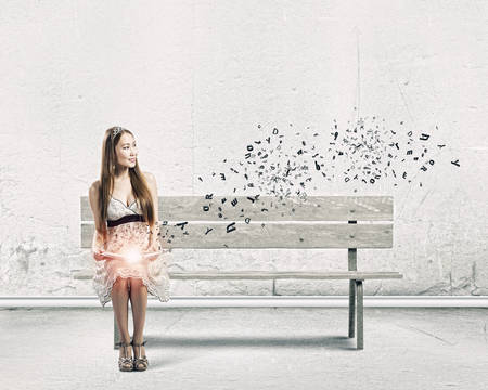 Young pretty asian woman sitting on bench and reading bookの写真素材