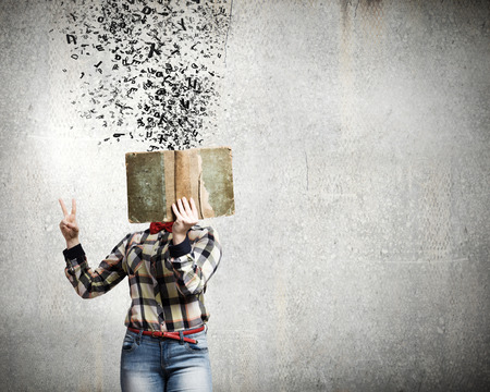 Woman in casual wear hiding her face behind bookの写真素材