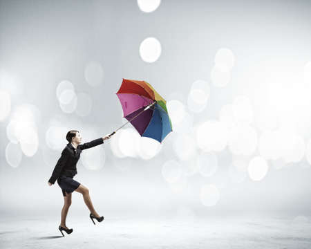 Young businesswoman walking with colorful umbrella against bokeh backgroundの写真素材