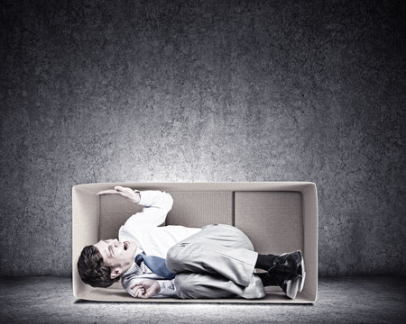 Young frustrated businessman sitting in small carton boxの写真素材