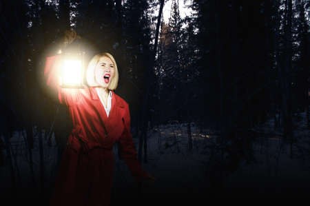 Young woman in red cloak with lantern lost in forestの写真素材