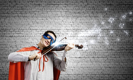 Young man in superhero costume playing violinの写真素材
