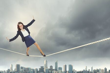 Young businesswoman balancing on rope above cityの写真素材