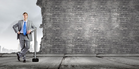 Young businessman with big hammer against wallの写真素材