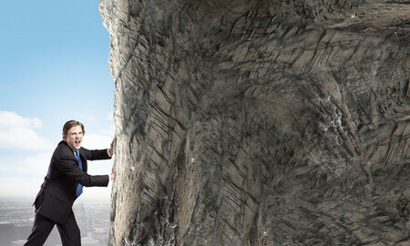 Young businessman making effort to move brick wallの写真素材