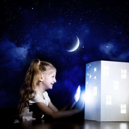 Cute little girl looking at model of house and dreamingの写真素材