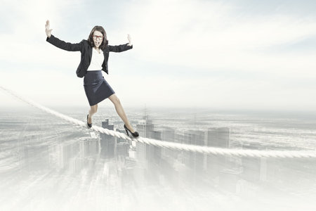 Young businesswoman balancing on rope above cityの写真素材