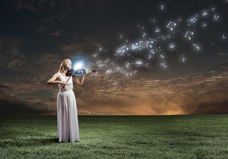 Young woman in white dress playing violin at nightの写真素材