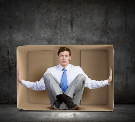Young frustrated businessman sitting in small carton boxの写真素材