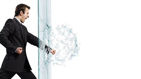 Young determined businessman breaking glass with karate punchの写真素材