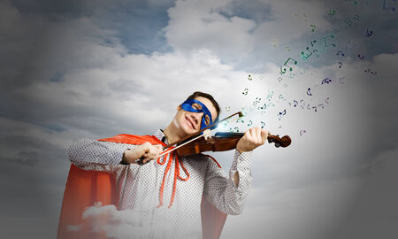Young man in superhero costume playing violinの写真素材