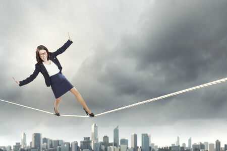 Young businesswoman balancing on rope above cityの写真素材