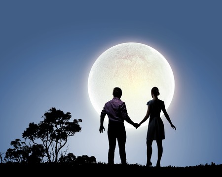 Silhouettes of couple against big moon at backgroundの写真素材