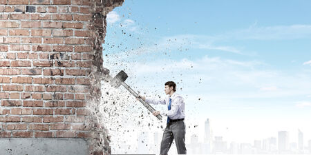 Young determined businessman with big hammer in hands crashing wallの写真素材