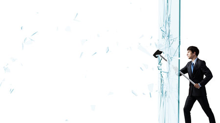 Young determined businessman breaking glass with hammerの写真素材