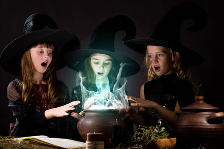 Three little Halloween witches reading spell above potの写真素材