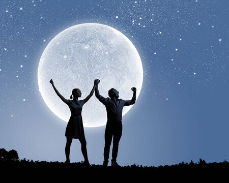Silhouettes of young couple against full moonの写真素材