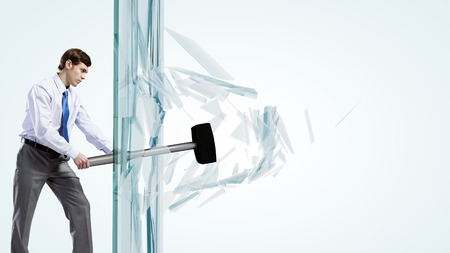 Young determined businessman breaking glass with hammerの写真素材