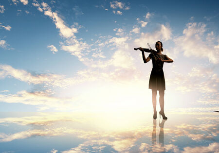 Silhouette of woman playing violin at sunsetの写真素材