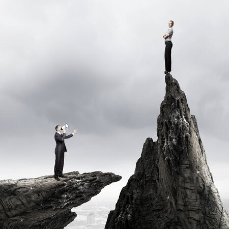 Businesswoman standing on top of rock and businessman screaming in megaphoneの写真素材