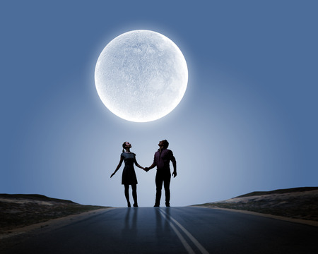 Silhouettes of couple against big moon at backgroundの写真素材