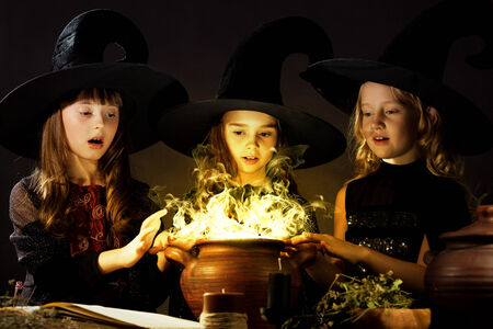Three little Halloween witches reading spell above potの写真素材