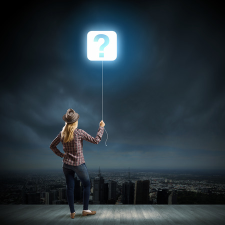 Young woman in casual holding balloon shaped like question markの写真素材