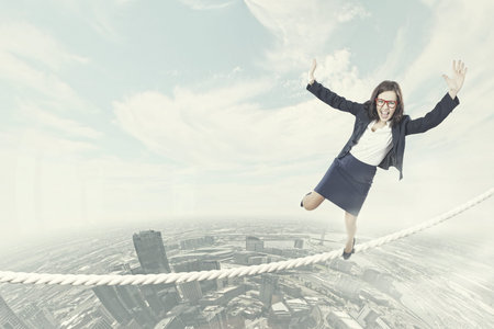 Young businesswoman balancing on rope above cityの写真素材