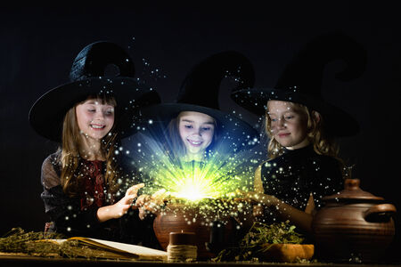 Three little Halloween witches reading spell above potの写真素材