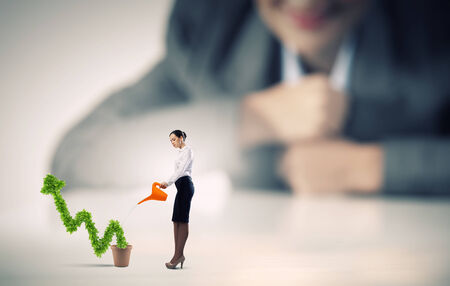 Businesswoman looking at miniature of woman watering plantの写真素材