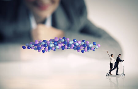 Businessman and businesswoman riding scooter with balloons in handの写真素材