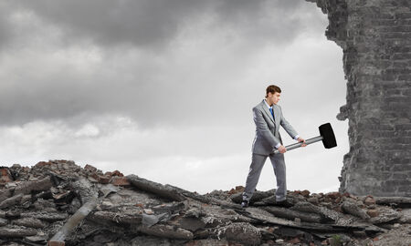 Young determined businessman with big hammer in hands crashing wallの写真素材