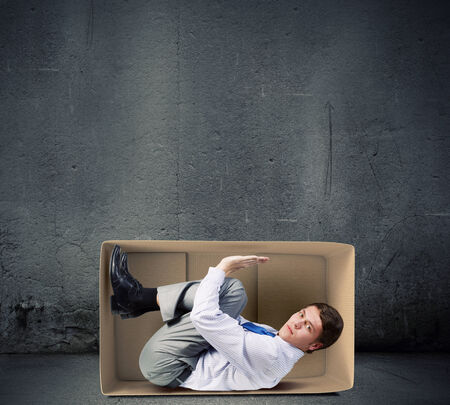 Young frustrated businessman trapped in small carton boxの写真素材